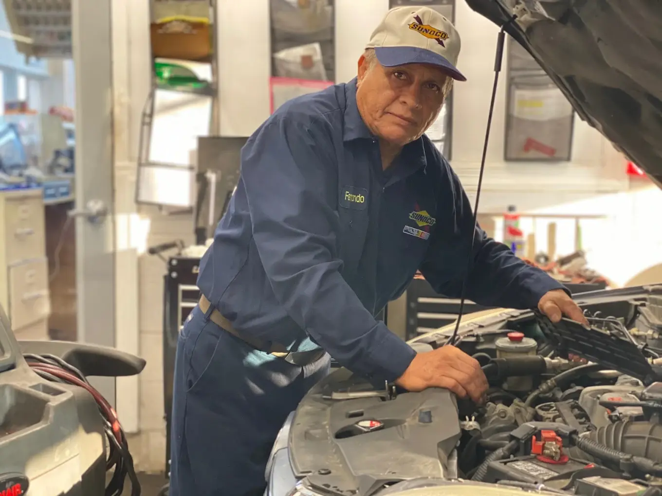 Technician under the hood at Rolling Road Sunoco in Springfield, checking how often a commuter car needs an oil change for severe driving