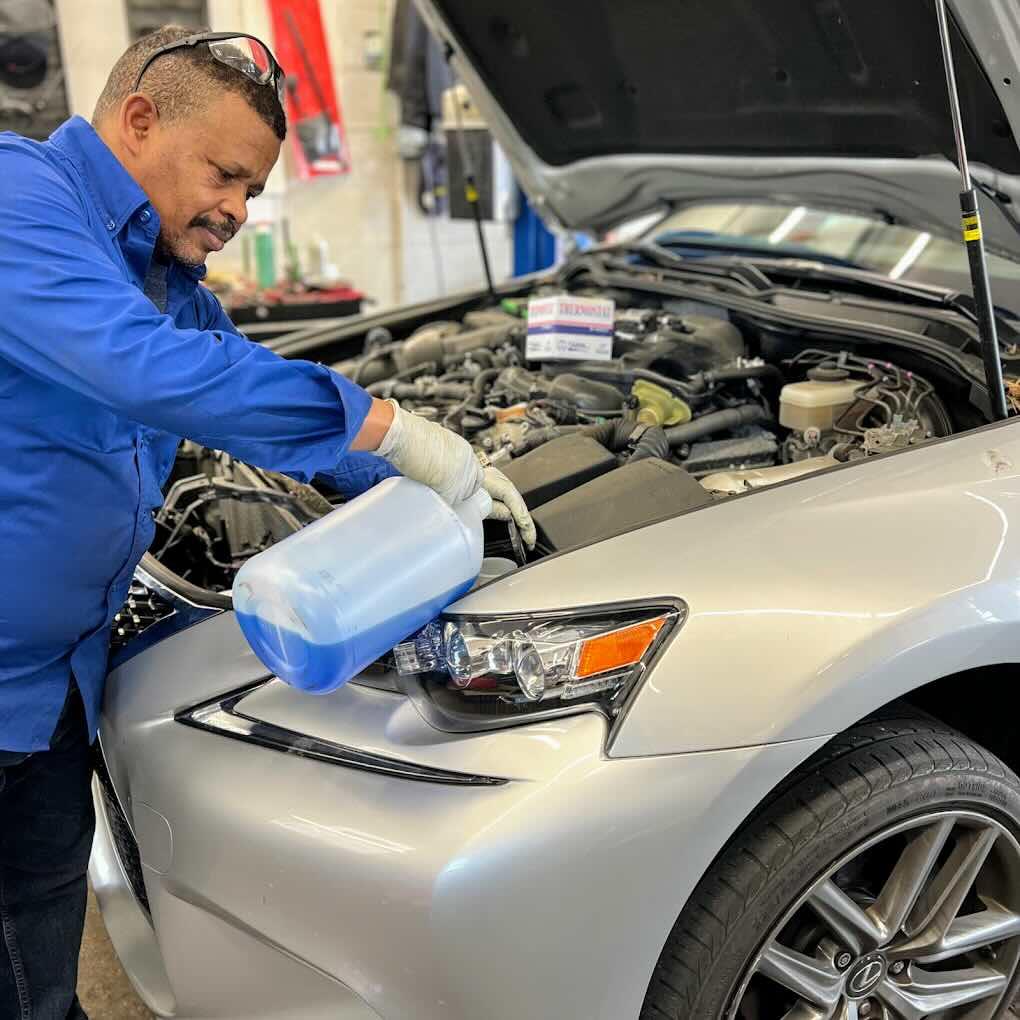 Technician topping off fluid under the hood during winter car maintenance for Northern Virginia roads at Rolling Road Sunoco in Springfield